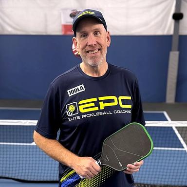 Jim Farrell in an EPC shirt and cap, holding a paddle on an indoor court