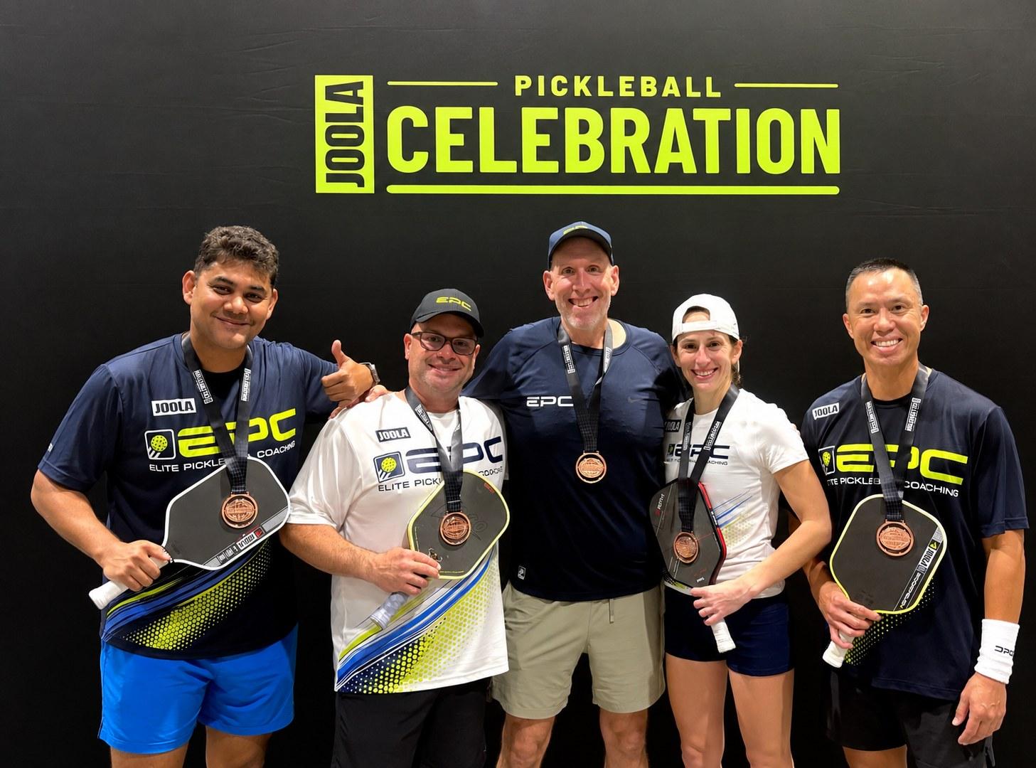 Jim Farrell with four EPC teammates, all wearing medals, in front of the JOOLA Pickleball Celebration backdrop